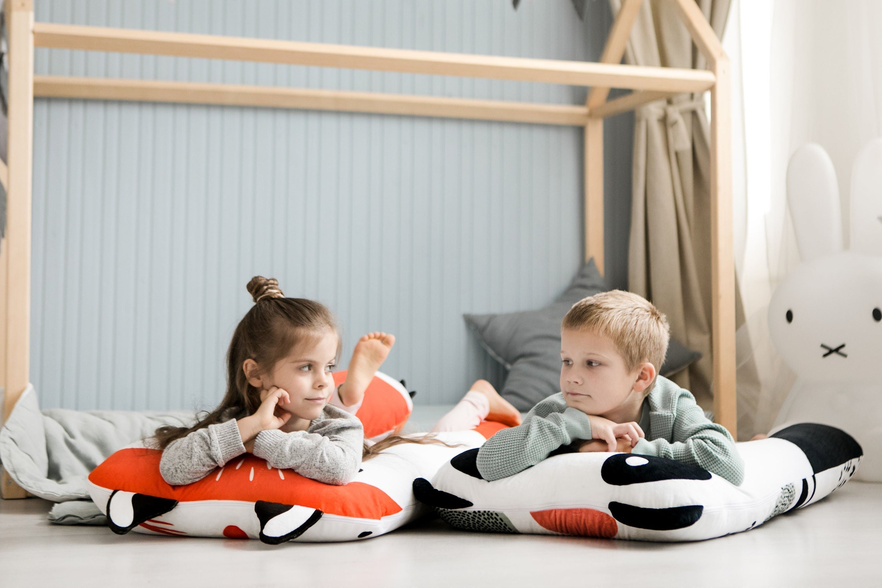Lachende kinderen liggen op een zacht vos- en panda-kinderkussen in hun kinderkamer